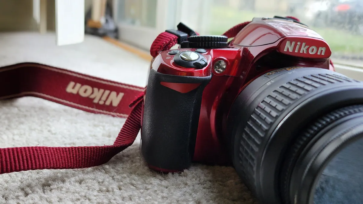 A red Nikon camera laying on beige carpet.